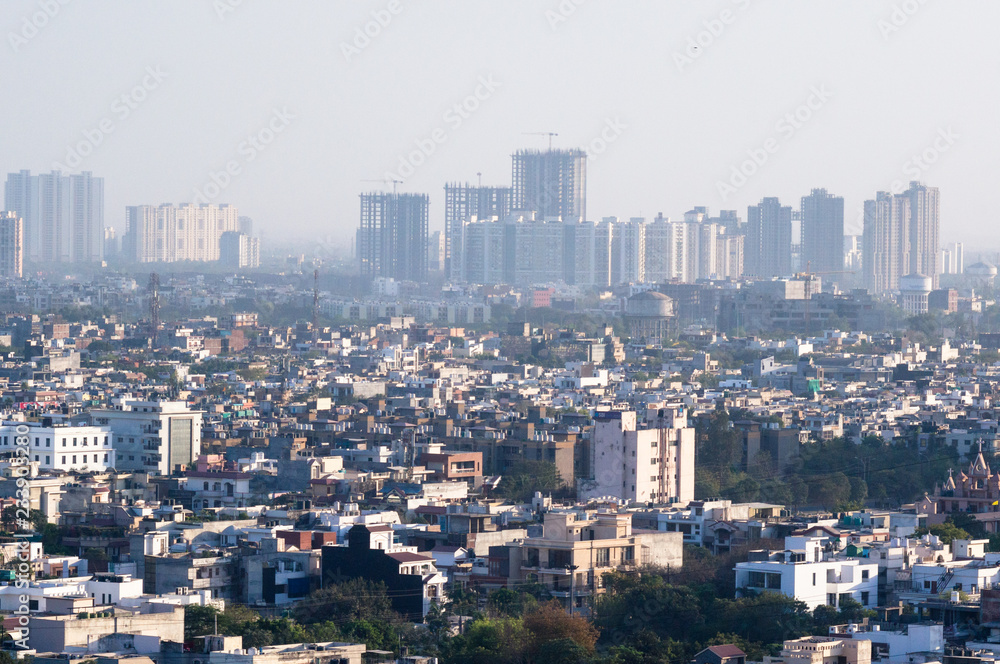 Aerial shot of cityscape with houses, offices and skyscrapers in the distance. Shows the crowded and messy nature of metro cities like Noida, Delhi, gurgaon, lucknow, jaipur, banaglore. Shows the fog