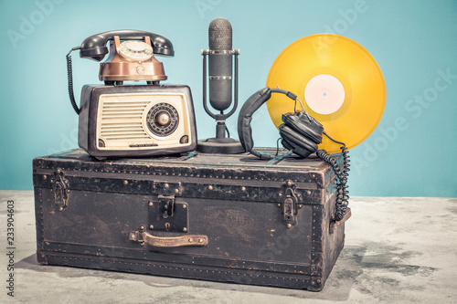 Fototapeta Radio retro z lat 60., stary miedziany telefon, mikrofon studyjny z lat 50. i płyta winylowa w kolorze złotym z lat 70., słuchawki na klasycznym bagażniku podróżnym. Filtrowane zdjęcie w stylu vintage