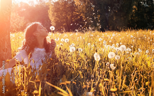 Teen blowing seeds from a dandelion flower in a park