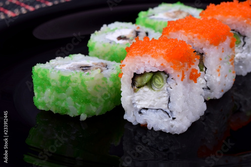 Fresh sushi rolls with cream cheese, rice, caviar and seafood against the black background. Asian cuisine meal