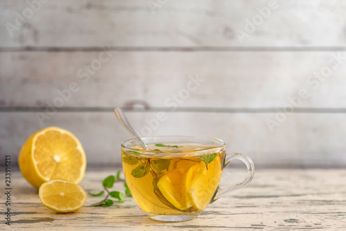 Cup of Lemon tea with lemon slices and mint on light wooden table