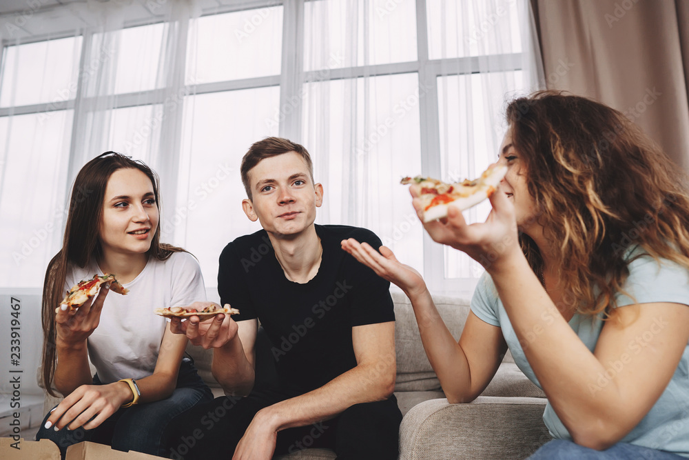cheerful friends hang out in living room enjoy pizza and chatting, young people talk having fun eating tasty food cheerful friends hang out in living room enjoy pizza and chatting, young people talk having fun eating tasty food