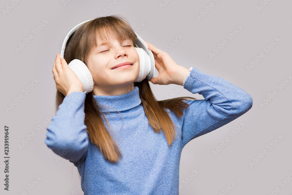Fototapeta premium Energy kid girl with headphones listening to music with closed eyes on white background