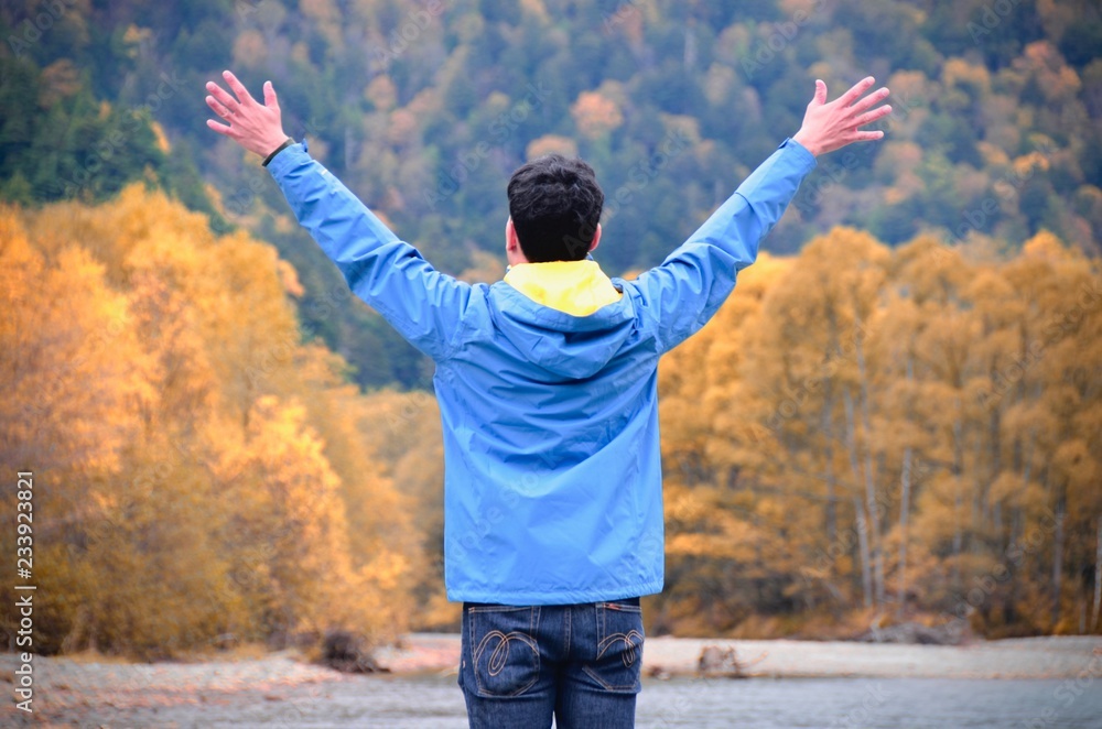 freedom man with hands up on the lake side against natural autumn forest and mountains