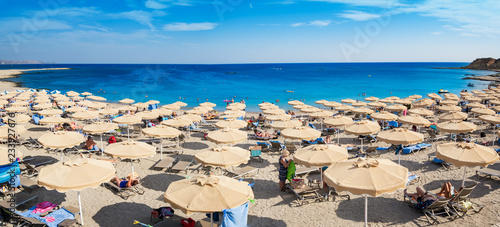 Fototapeta Naklejka Na Ścianę i Meble -   Kiotari beach with umbrellas and holiday-makers in village of Kiotari - PANORAMA (Rhodes, Greece)