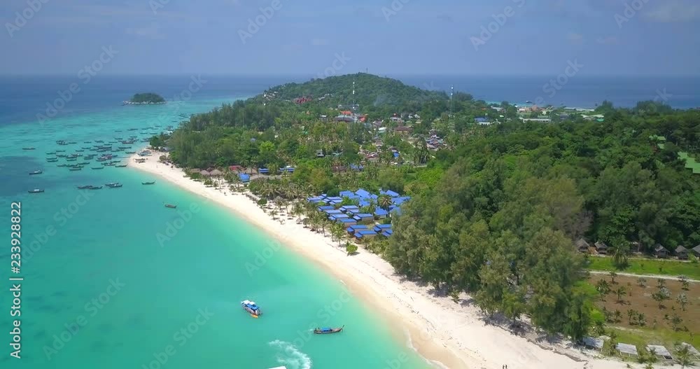 Forward advancing aerial drone view descending from high above crystal clear tropical ocean water to white sand Sunrise Beach on sunny day in travel destination island Ko Lipe, Thailand. 4k 23.976fps Forward advancing aerial drone view descending from high above crystal clear tropical ocean water to white sand Sunrise Beach on sunny day in travel destination island Ko Lipe, Thailand. 4k 23.976fps