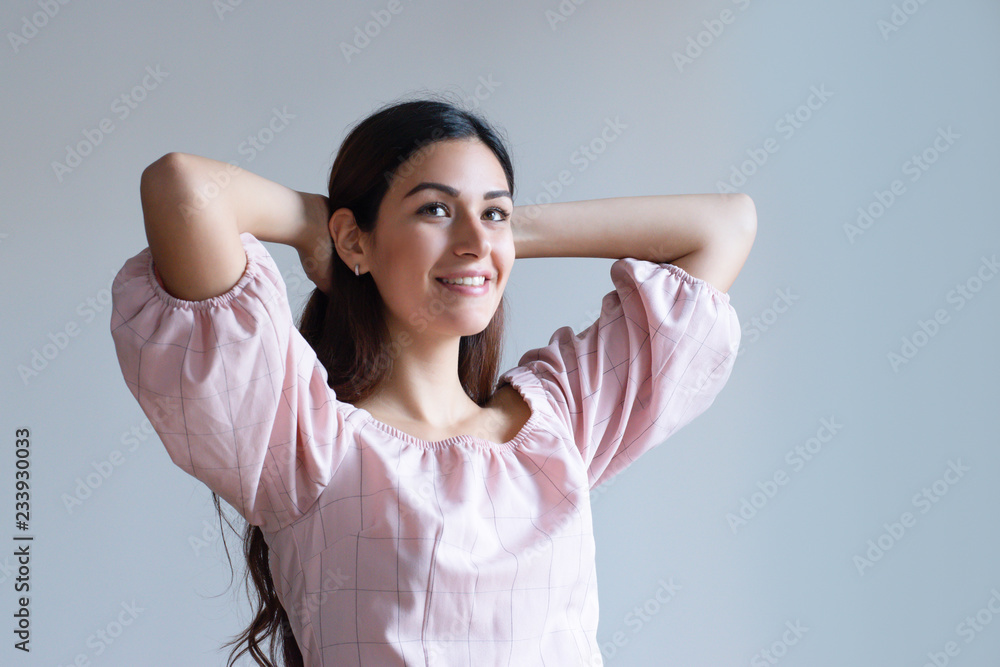 Smiling pretty Caucasian girl holding hands behind hand. Young female student in light pink top imagining new hairstyle. Dreaming about prom concept Smiling pretty Caucasian girl holding hands behind hand. Young female student in light pink top imagining new hairstyle. Dreaming about prom concept