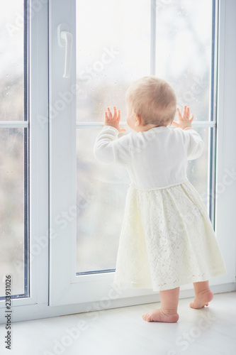 blonde curly toddler Baby girl looking through a window.