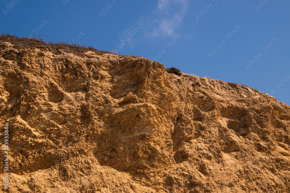 Rugged jagged brown cliff edge. There is a deep blue sky background with broken puffy cloud