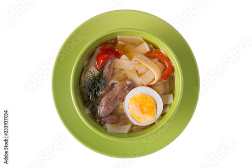 Chicken soup with noodels, meat pieces, herbs and egg in bowl on white background. Top view