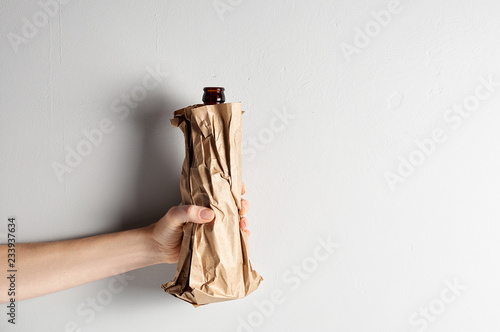 Hand holding beer bottle in the paper bag on gray concrete background
