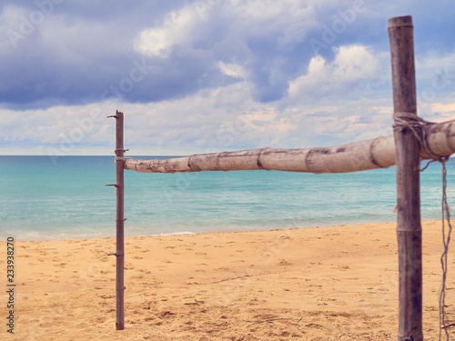 The wooden crossbar is located on a tropical beach. In the distance you can see the sea or the ocean and the sky with clouds.
