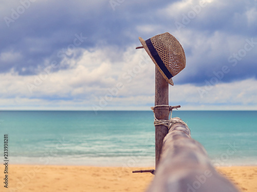 The wooden crossbar is located on a tropical beach. In the distance you can see the sea or the ocean and the sky with clouds. There is a straw hat on a wooden stand.