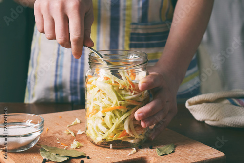 Woman cook sauerkraut or salad on wooden background. Step 5 - Put the cabbage in the jars. Fermented preserved vegetables food concept.