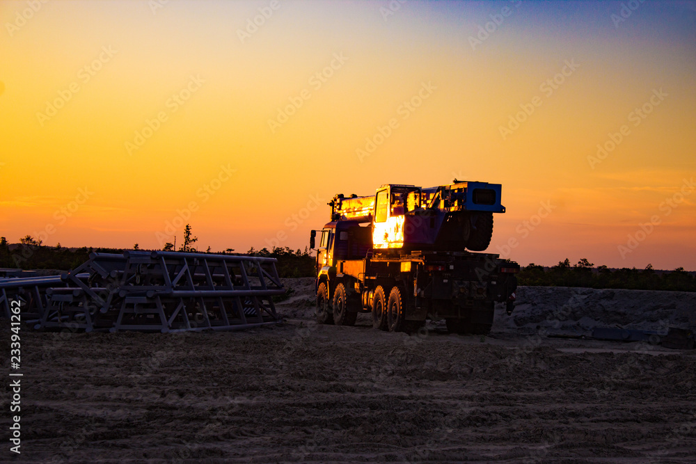 Fototapeta premium all-terrain truck-mounted crane at a construction site in the background of the sunset