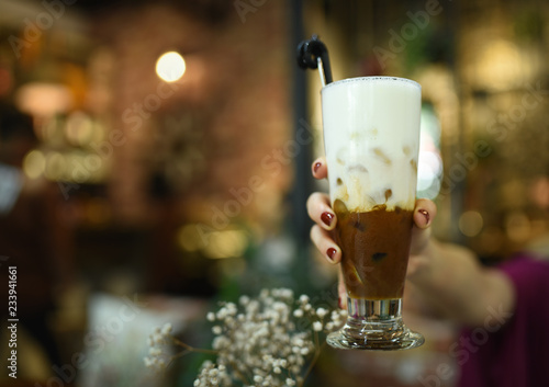 Ice coconut coffee in woman hand at coffee shop. A cup of layer coffee and milk holding by a girl with red color nails. Vintage coffee shop. Testy mocha coffee with milk.