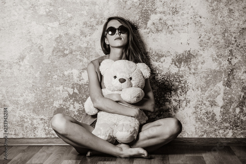 Sad grunge girl near wall with teddy bear. Image in black and white color style