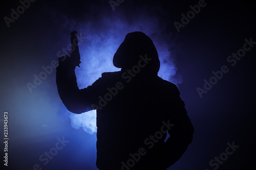 Silhouette of man with assault rifle ready to attack on dark toned foggy background or dangerous bandit in black wearing balaclava and holding gun in hand. Shooting terrorist with weapon theme decor