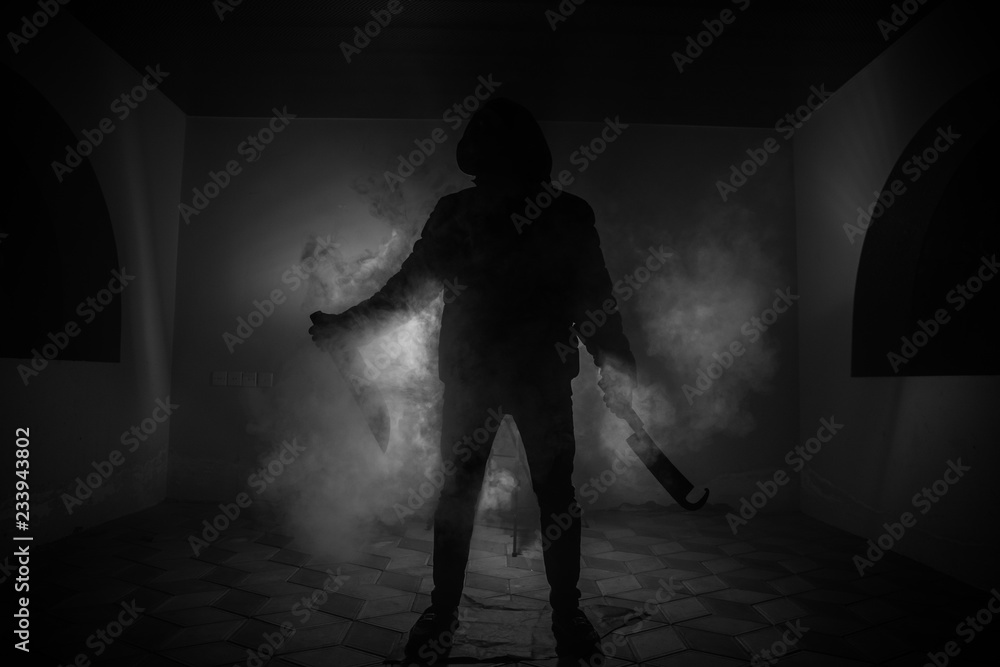 A dangerous hooded man standing in the dark and holding a knife. Face can not be seen. Committing a crime concept. Selective focus