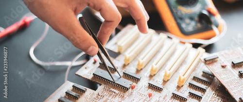 close up hands reapair the electric board with tweezers f photo