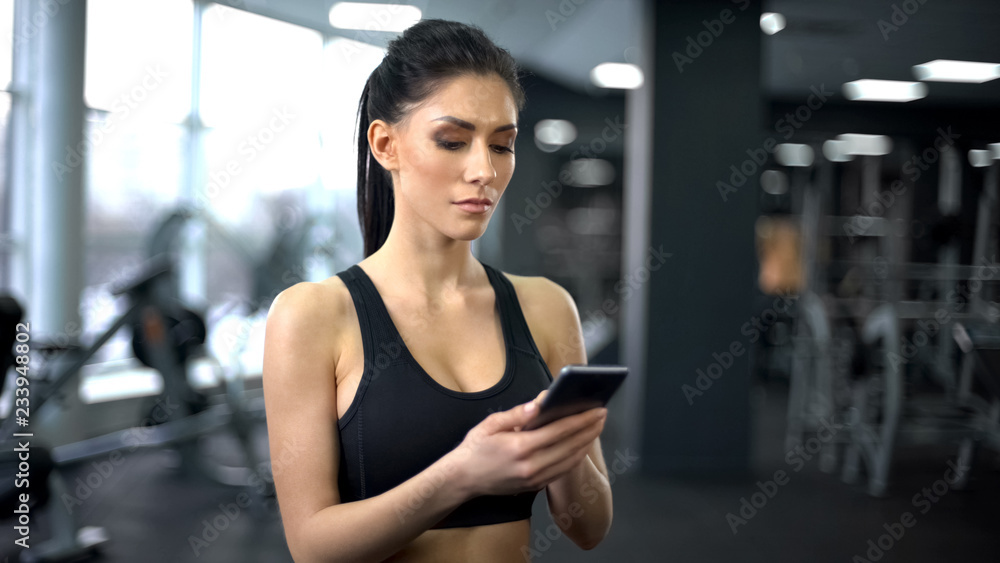 Fototapeta premium Purposeful lady in sportswear scrolling smartphone application, motivation