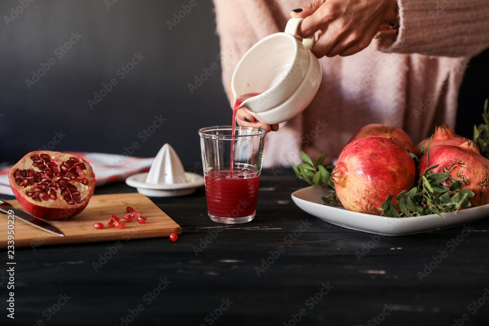 Φωτογραφία Woman pours freshly squeezed pomegranate juice in a glass near ingredients on black wooden background