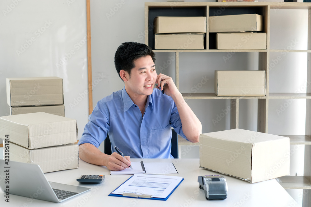 Fototapeta premium Young male business owner working at home, taking customer orders by phone.