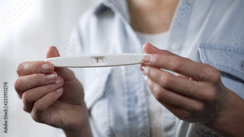 Female holding negative pregnancy test in hands, demonstrating before camera photo