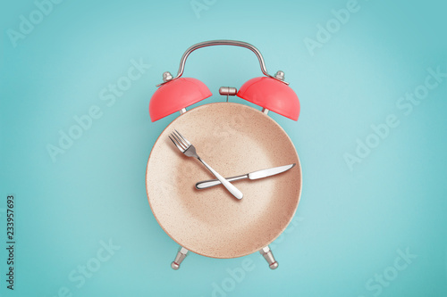 Alarm clock and plate with cutlery . Concept of intermittent fasting, lunchtime, diet and weight loss photo
