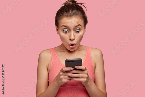 Photos Stupefied emotional woman stares with bugged eyes at smart phone, feels shocked