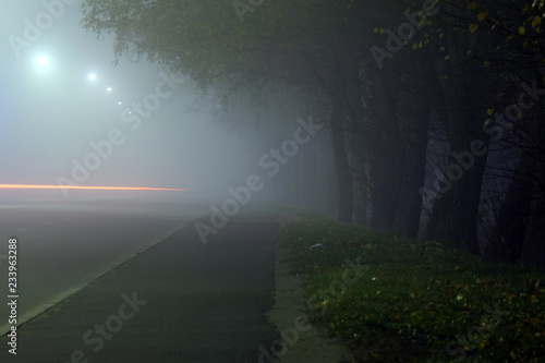 city street at night in heavy fog, traces of headlights of cars on a long exposure