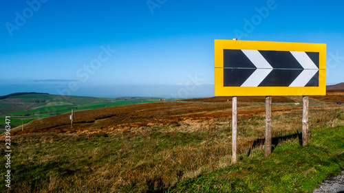 Road sign indicating a sharp deviation on the A537 in the beautiful Peak District between Buxton and Macclesfield in Derbyshire, England. Taken on a sunny day showing blue sky & green fields and hills