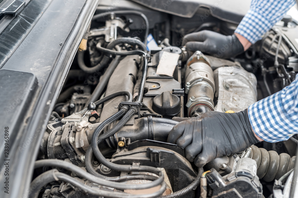 Car engine with worker's hands in gloves