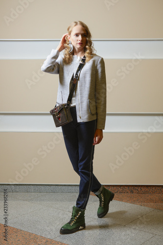 Cute student girl in jacket, jeans and boots with shoulder bag ondoors photo