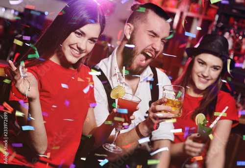 A group of friends at a party in a nightclub clink glasses with alcoholic beverages.