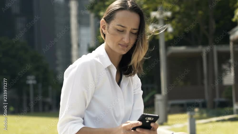 Young, pretty businesswoman texting on smartphone on bench in city Young, pretty businesswoman texting on smartphone on bench in city