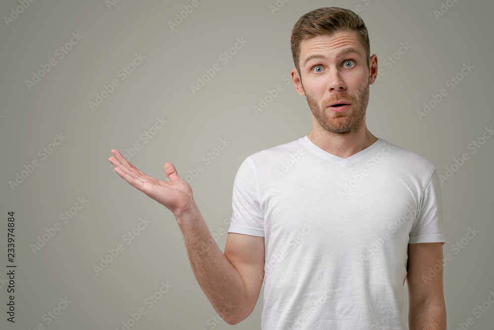 A horizontal portrait of attractive unshaven man with a lowered jaw, raises his palm, shows something amazing. Bearded student shows space for your promotional content or promotion A horizontal portrait of attractive unshaven man with a lowered jaw, raises his palm, shows something amazing. Bearded student shows space for your promotional content or promotion