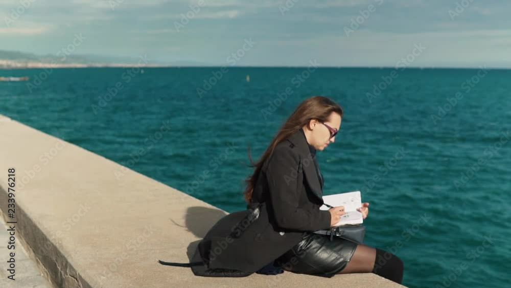 Woman drawing sketches in her sketchbook outdoors near the sea. slowmotion shot. Woman drawing sketches in her sketchbook outdoors near the sea. slowmotion shot.