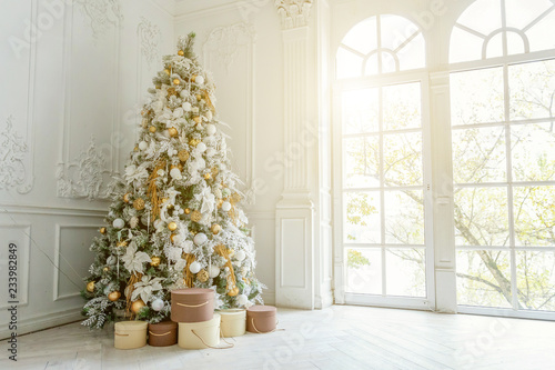 Classic christmas New Year decorated interior room New year tree. Christmas tree with gold decorations. Modern white classical style interior design apartment, large window. Christmas eve at home