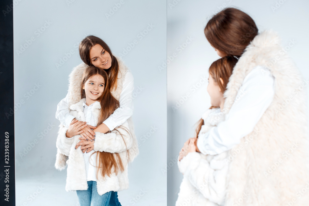 Stylish beautiful mother and a cute daughter with blue eyes in studio hugging and having fun Stylish beautiful mother and a cute daughter with blue eyes in studio hugging and having fun