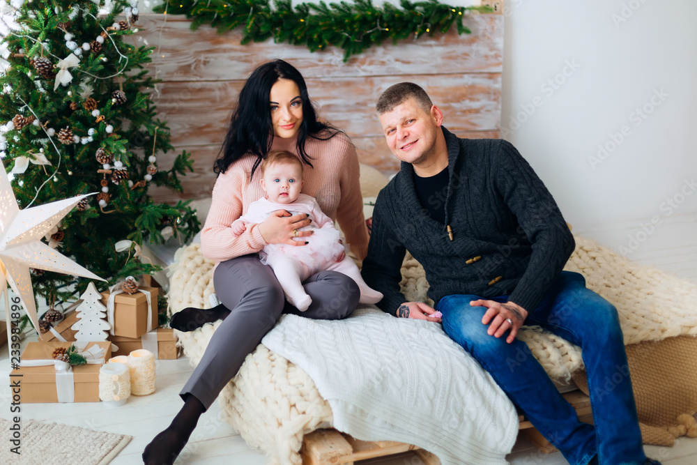 the parents with the baby sit on the bed and look at the camera lens on christmas-themed room the parents with the baby sit on the bed and look at the camera lens on christmas-themed room
