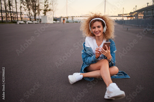 Beautiful and cheerful young woman with lush hair, outdoors. Charming curly hair in a denim jacket.