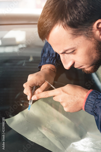 Close-up of a professional windshield repairman fills a crack in the glass with a special polymer through a syringe. Elimination of cracks and chips on windshields