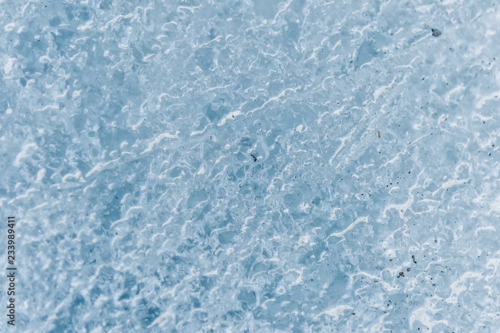 A close-up of the surface of a fragment of a glacier with a structure of strips and bubbles interspersed with sand and rocky rock. Ice blue texture to the light. Small DOF