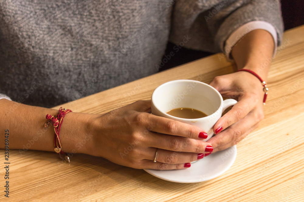 White cup of coffee in female hands. Warm your hands with a cup of hot drink. Meeting in a cafe. The girl in the coffee shop. Morning coffee in the restaurant. Red thread in the bracelet on hand. White cup of coffee in female hands. Warm your hands with a cup of hot drink. Meeting in a cafe. The girl in the coffee shop. Morning coffee in the restaurant. Red thread in the bracelet on hand.
