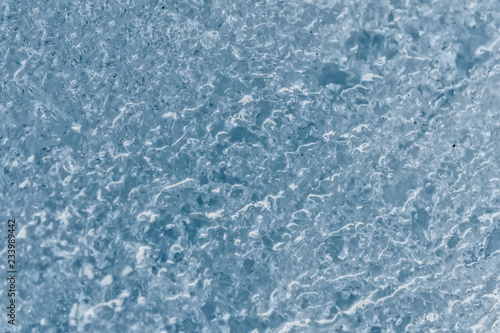 Close-up of the surface of a fragment of a glacier with a structure of stripes and bubbles. Ice blue texture to the light. Small DOF