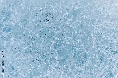 A close-up of the surface of a fragment of a glacier with a structure of strips and bubbles interspersed with sand and rocky rock. Ice blue texture to the light. Small DOF