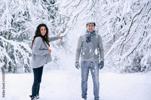 Happy beautiful pregnant woman in warm clothes throws snow on her husband. Couple in love having fun in winter park.