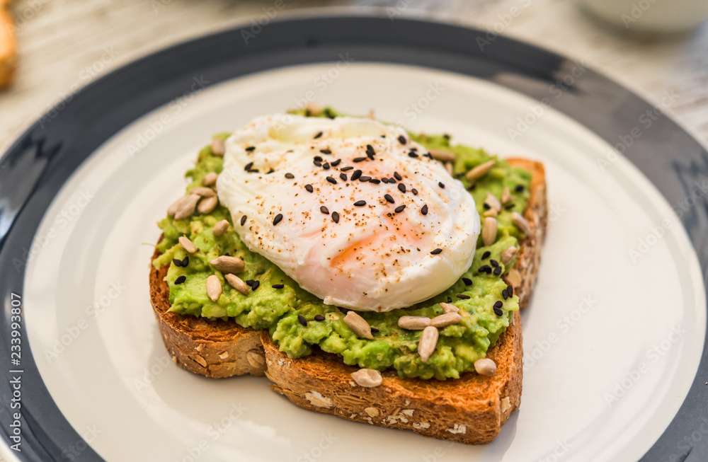 Close up food photography of an avocado toast with poached egg and sesame seeds. Breakfast, lunch, brunch, light dinner dish meal, vegetarian food, healthy eating concept.