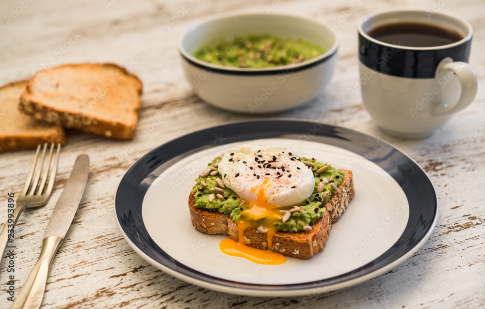 Food photography of an avocado toast with poached egg, sesame seeds, and black coffee. Breakfast, lunch, brunch, light dinner dish meal, vegetarian food, healthy eating concept.